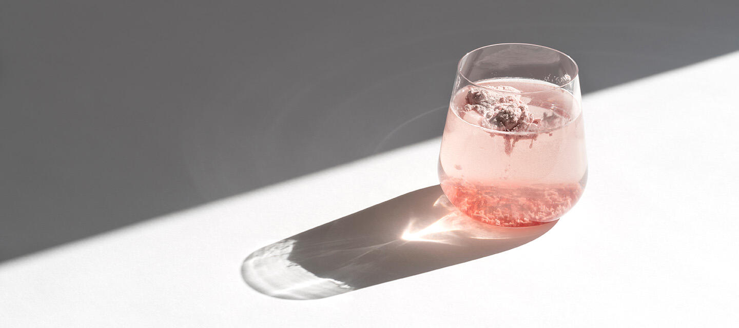 A glass filled with water and pink powder on a white surface
